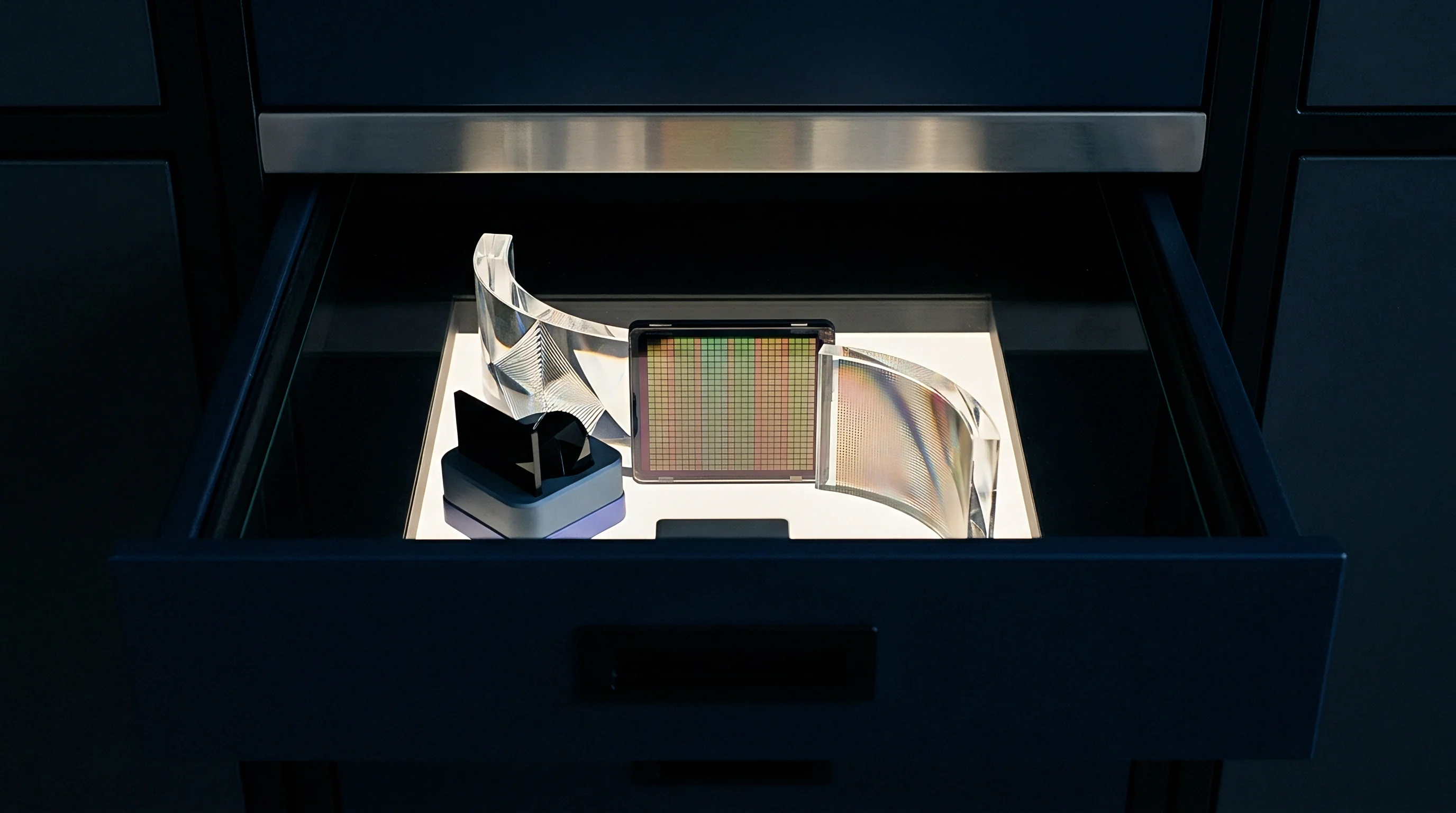 Silicon image sensor matrix and transparent optical prisms rest inside an illuminated drawer during precision assembly.
